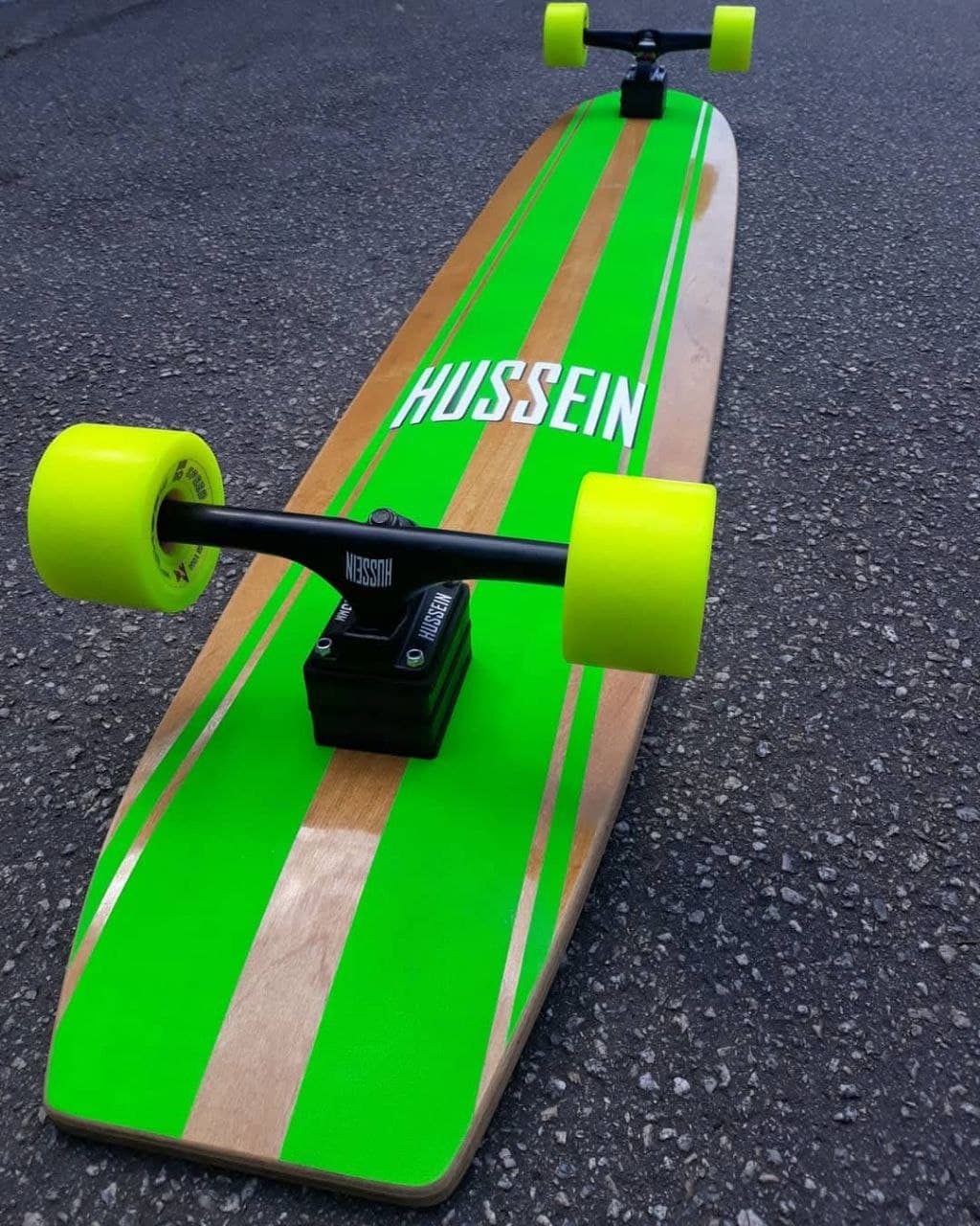 Longboard verde apoiado na grama — shape clássico Hussein