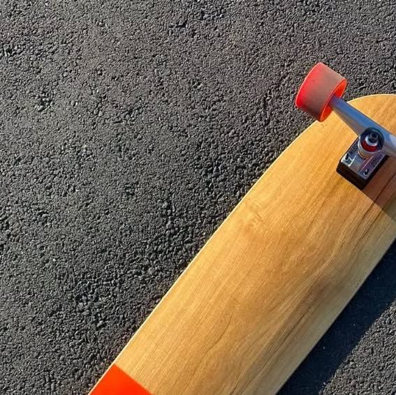 Longboard deck close-up on asphalt — orange accents, red wheels