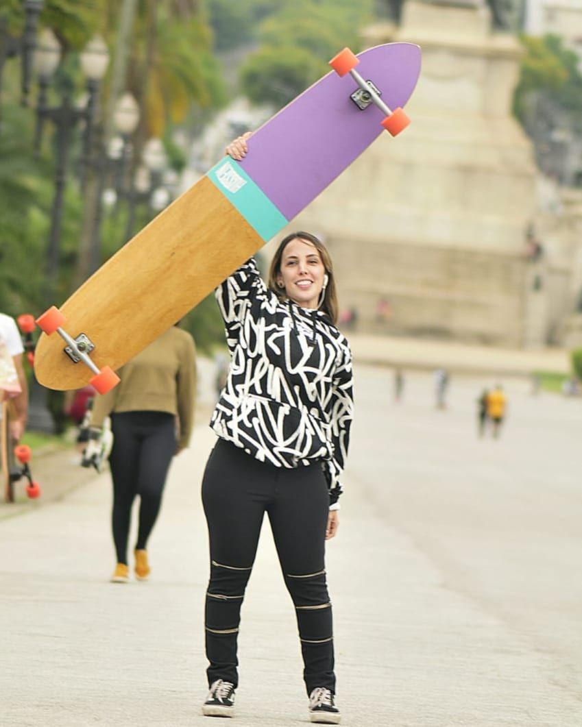 Woman holding longboard with orange wheels — palm trees